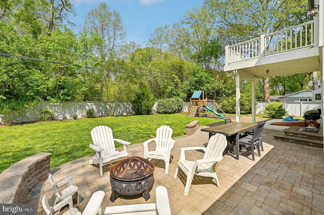 view of patio with outdoor dining space, grilling area, a playground, a fire pit, and a fenced backyard