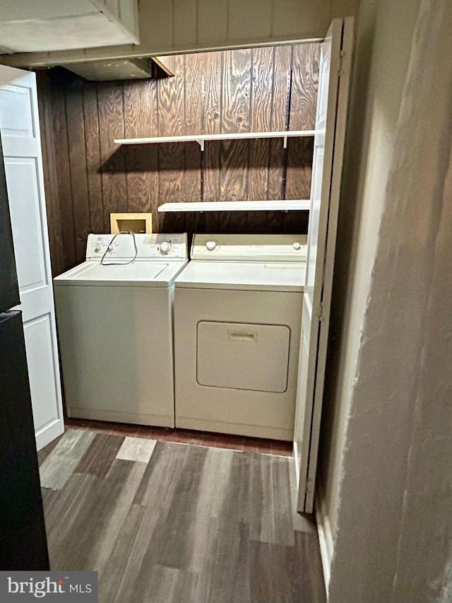 laundry area with separate washer and dryer, laundry area, wooden walls, and wood finished floors