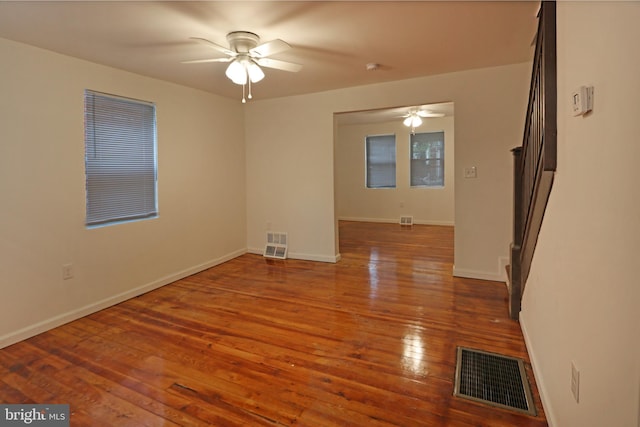 empty room with wood-type flooring, ceiling fan, visible vents, and baseboards