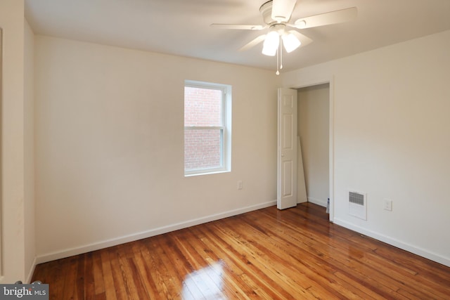 spare room with wood-type flooring, a ceiling fan, baseboards, and visible vents