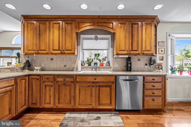 kitchen featuring stainless steel dishwasher, light stone countertops, light wood-style floors, brown cabinets, and a sink