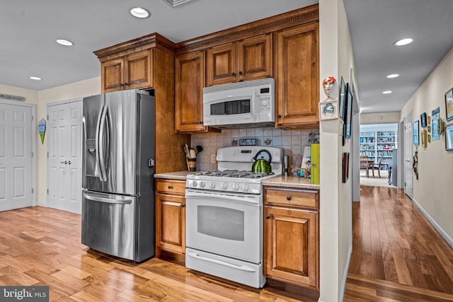 kitchen featuring brown cabinetry, recessed lighting, light wood-style floors, and white appliances