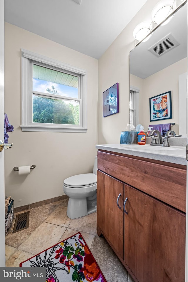 half bathroom with vanity, baseboards, toilet, and visible vents