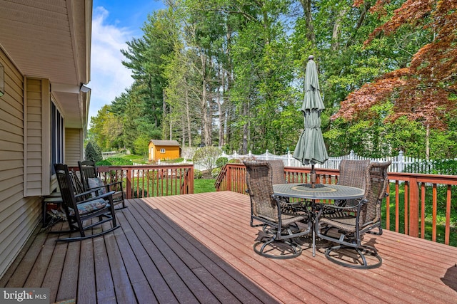 wooden deck featuring a storage shed, an outbuilding, outdoor dining space, and a fenced backyard