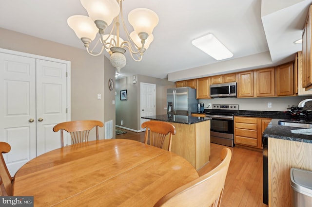 kitchen with appliances with stainless steel finishes, a center island, a sink, an inviting chandelier, and light wood-style flooring