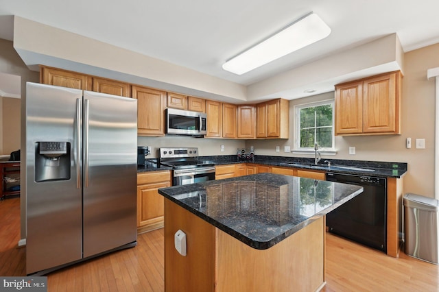 kitchen with dark stone countertops, a center island, a sink, light wood-style flooring, and stainless steel appliances