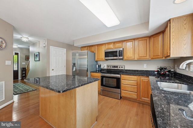 kitchen featuring appliances with stainless steel finishes, a sink, light wood finished floors, dark stone countertops, and a center island