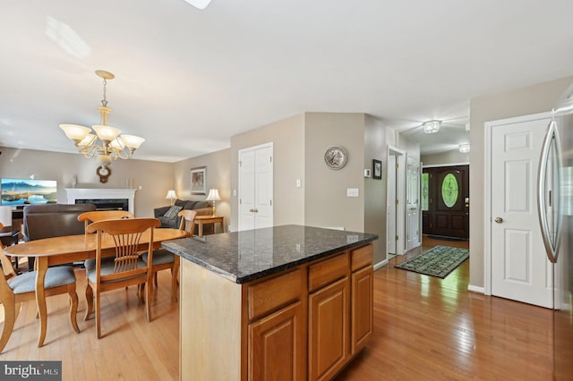 kitchen with an inviting chandelier, a kitchen island, a high end fireplace, open floor plan, and light wood-style floors