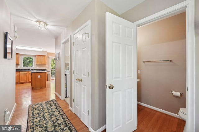 corridor featuring baseboards, a sink, and light wood finished floors