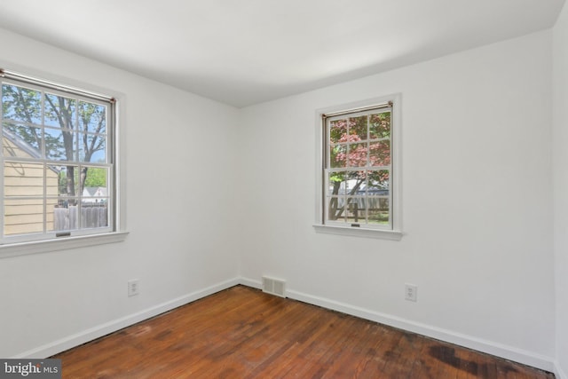spare room featuring baseboards, visible vents, a healthy amount of sunlight, and dark wood-type flooring