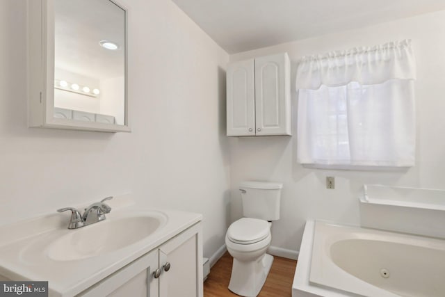 bathroom with vanity, wood finished floors, toilet, a tub with jets, and baseboards