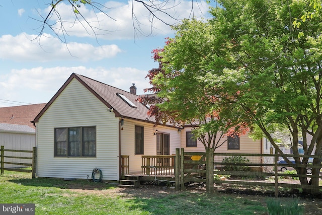 back of house with a chimney, a lawn, a wooden deck, fence, and a shingled roof