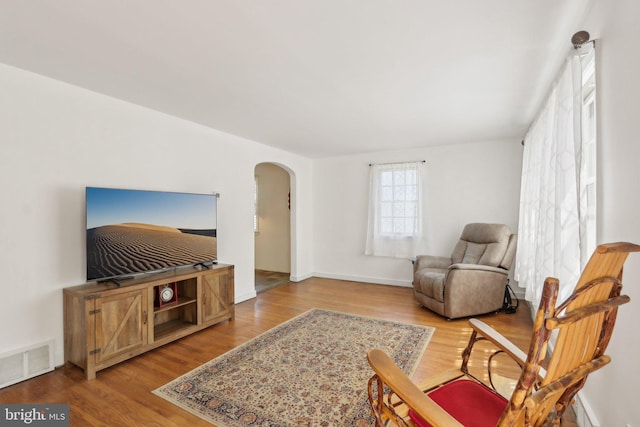 living room with arched walkways, baseboards, visible vents, and wood finished floors