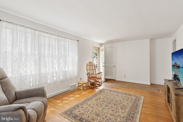 living area with baseboards, light wood-style flooring, and visible vents