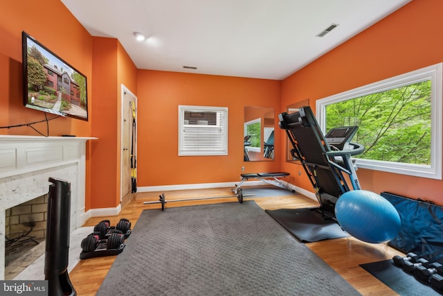 exercise area with visible vents, wood finished floors, baseboards, and a fireplace with flush hearth