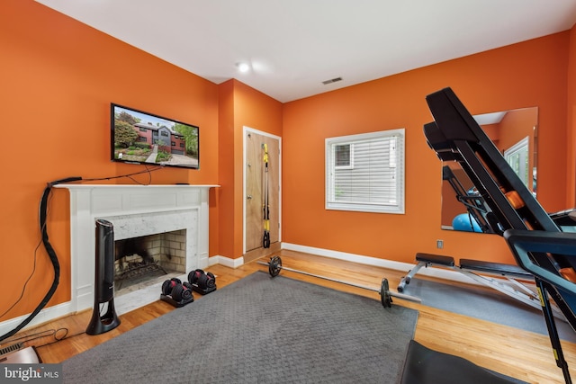 exercise room featuring a fireplace, baseboards, visible vents, and wood finished floors