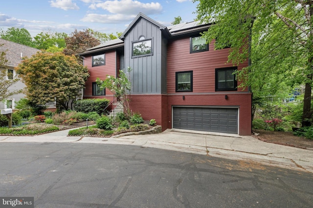 view of front of property featuring an attached garage, brick siding, driveway, solar panels, and board and batten siding