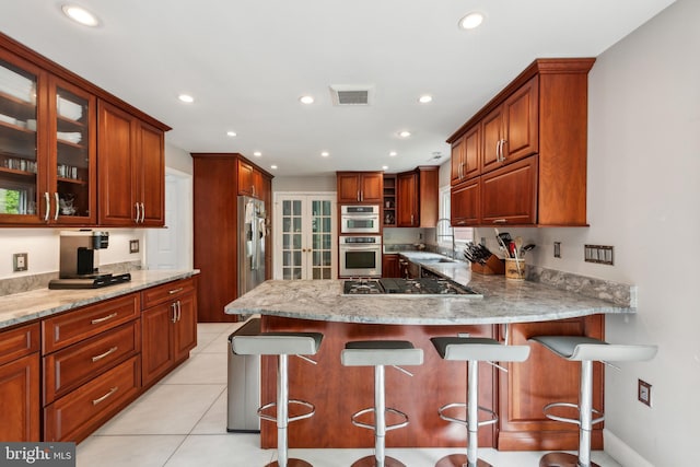 kitchen with stainless steel appliances, a peninsula, visible vents, and glass insert cabinets