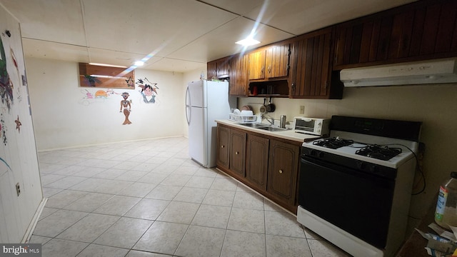 kitchen with light tile patterned floors, gas range oven, light countertops, freestanding refrigerator, and under cabinet range hood