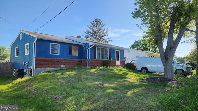 ranch-style home with a chimney, brick siding, fence, central AC unit, and a front yard