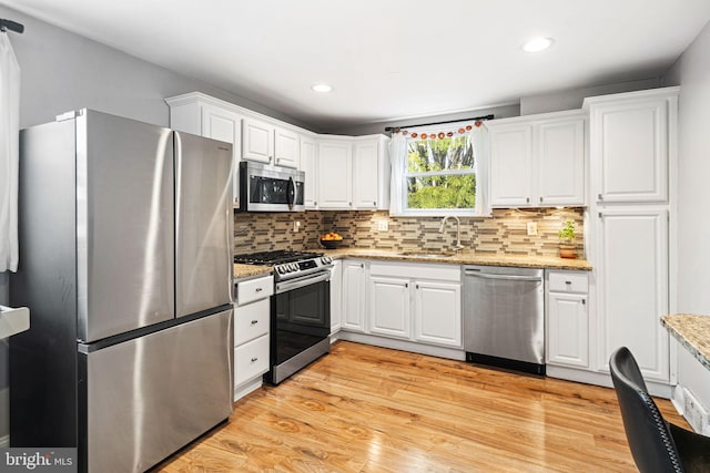 kitchen featuring appliances with stainless steel finishes, tasteful backsplash, a sink, light wood finished floors, and white cabinetry
