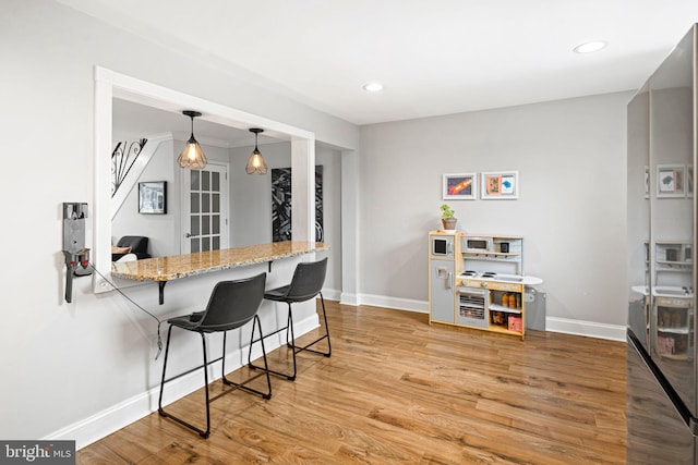 kitchen featuring a kitchen bar, wood finished floors, baseboards, light stone counters, and recessed lighting
