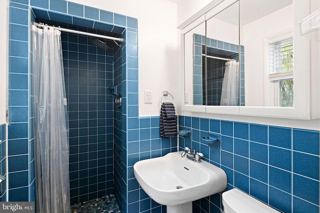bathroom with a sink, toilet, a wainscoted wall, tile walls, and tiled shower