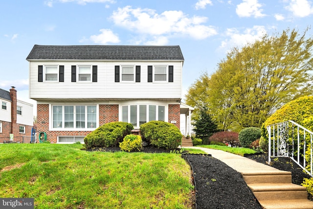 colonial-style house with a shingled roof, a front yard, and brick siding