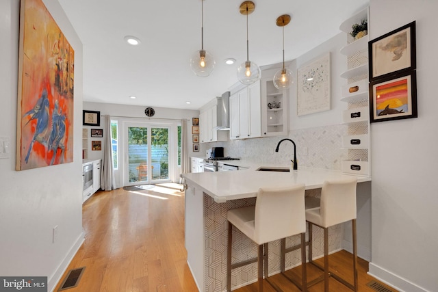 kitchen with white cabinets, a sink, wall chimney exhaust hood, baseboards, and backsplash