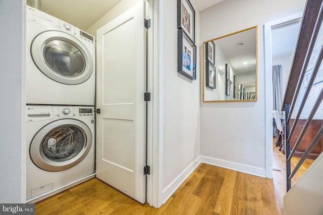 laundry area with baseboards, stacked washer and clothes dryer, light wood-style flooring, and laundry area