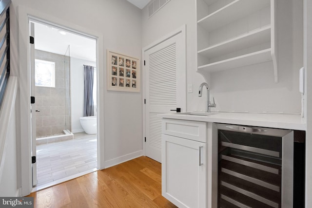 bar featuring a sink, wet bar, light wood-type flooring, wine cooler, and visible vents