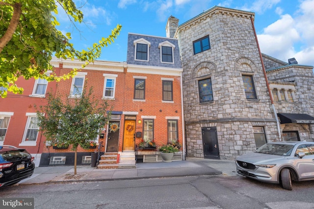 view of property featuring a high end roof, mansard roof, and brick siding