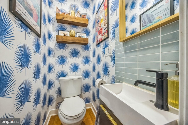 half bathroom featuring vanity, toilet, baseboards, wallpapered walls, and wood finished floors