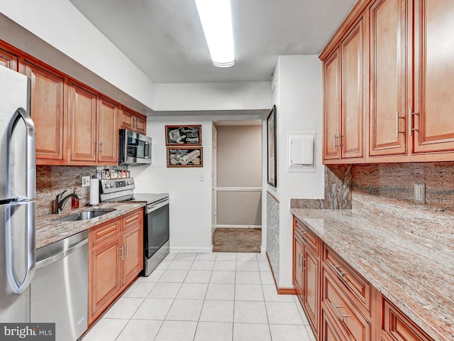 kitchen with decorative backsplash, light stone countertops, baseboards, a sink, and appliances with stainless steel finishes