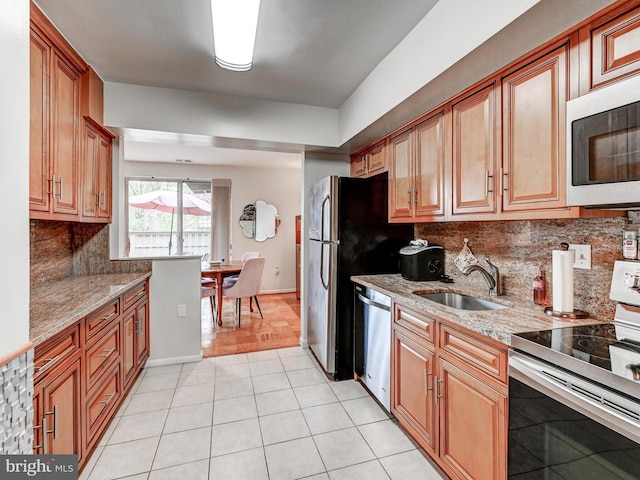 kitchen with appliances with stainless steel finishes, light stone counters, a sink, light tile patterned floors, and backsplash