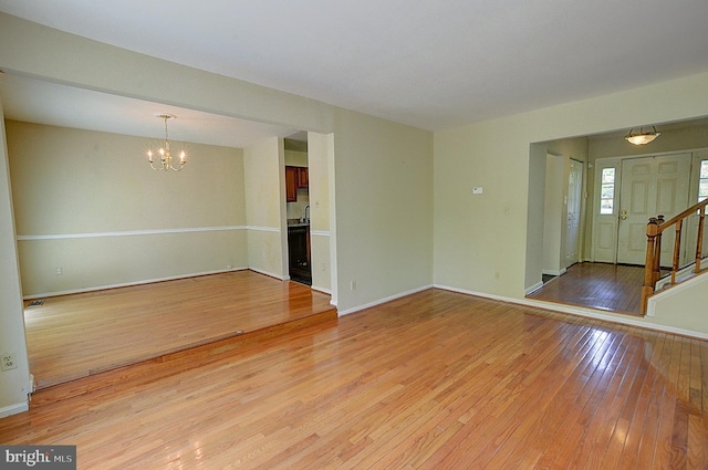 spare room featuring light wood finished floors, a chandelier, stairway, and baseboards