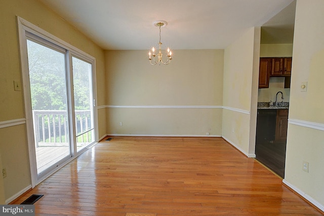 unfurnished dining area with a sink, a chandelier, light wood finished floors, and baseboards