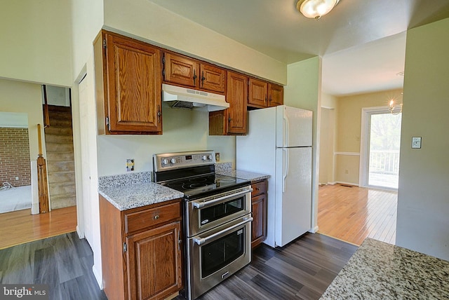 kitchen with under cabinet range hood, range with two ovens, dark wood-style floors, freestanding refrigerator, and brown cabinets
