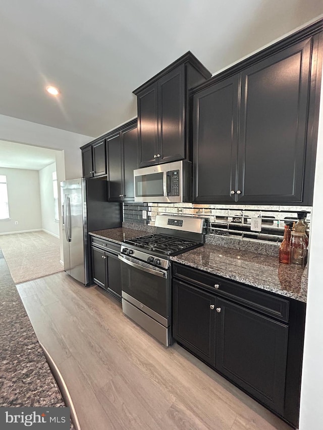 1108 Dovetail Cir, Fredericksburg, VA 22401 - kitchen with stainless steel appliances, dark cabinets, decorative backsplash, light wood-type flooring, and dark stone counters