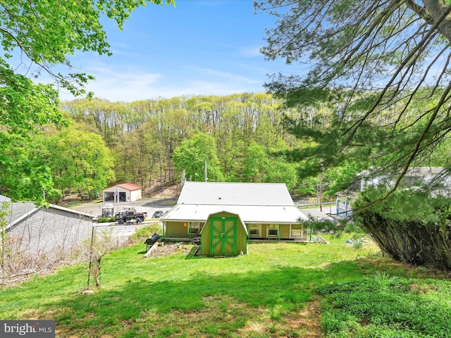 view of yard with a storage shed, a wooded view, and an outbuilding