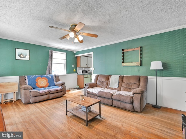 living room with crown molding, a ceiling fan, light wood finished floors, and a textured ceiling