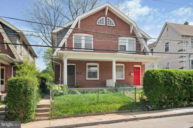 colonial inspired home with a gambrel roof, a fenced front yard, a porch, and brick siding