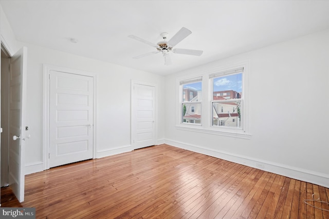 unfurnished bedroom featuring ceiling fan, light wood-style floors, baseboards, and multiple closets
