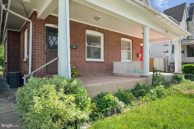 property entrance with a porch, brick siding, and fence