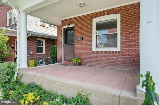 entrance to property featuring a porch and brick siding
