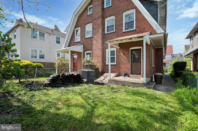 rear view of property with a yard, brick siding, fence, and central air condition unit