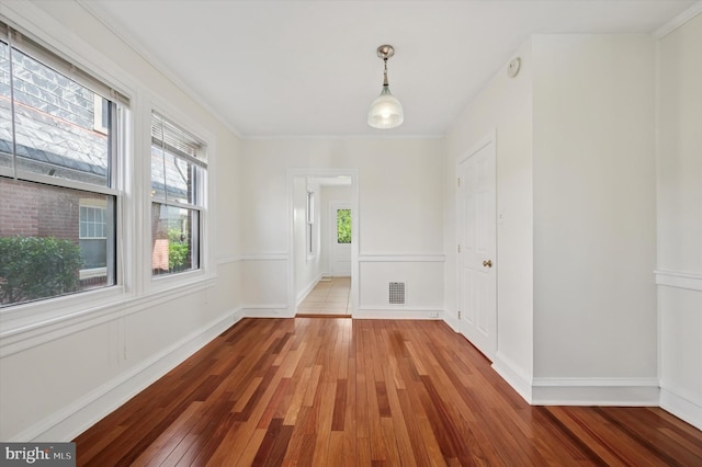 unfurnished dining area featuring baseboards, crown molding, wood-type flooring, and visible vents