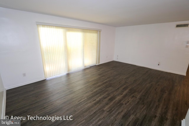 unfurnished room with baseboards, dark wood-style floors, and visible vents