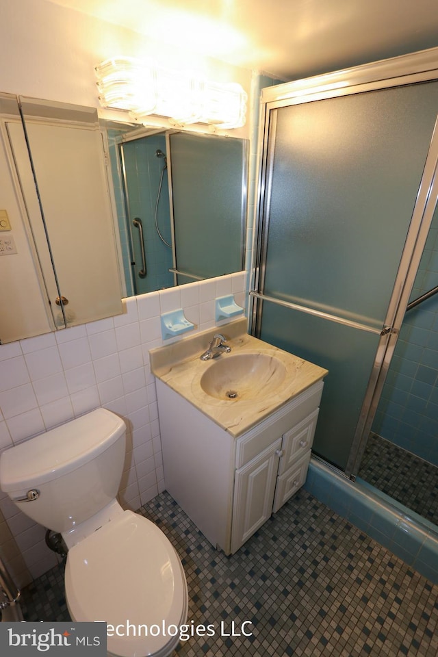bathroom with tile patterned flooring, vanity, toilet, tile walls, and a stall shower