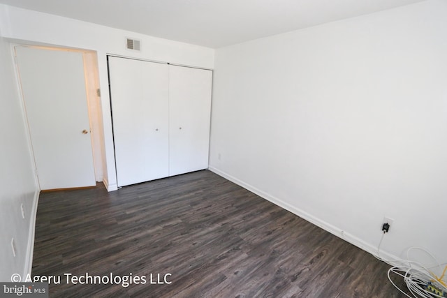unfurnished bedroom featuring a closet, baseboards, dark wood-type flooring, and visible vents